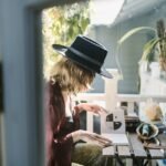 A woman in a hat reading tarot cards on a sunlit balcony surrounded by crystals.